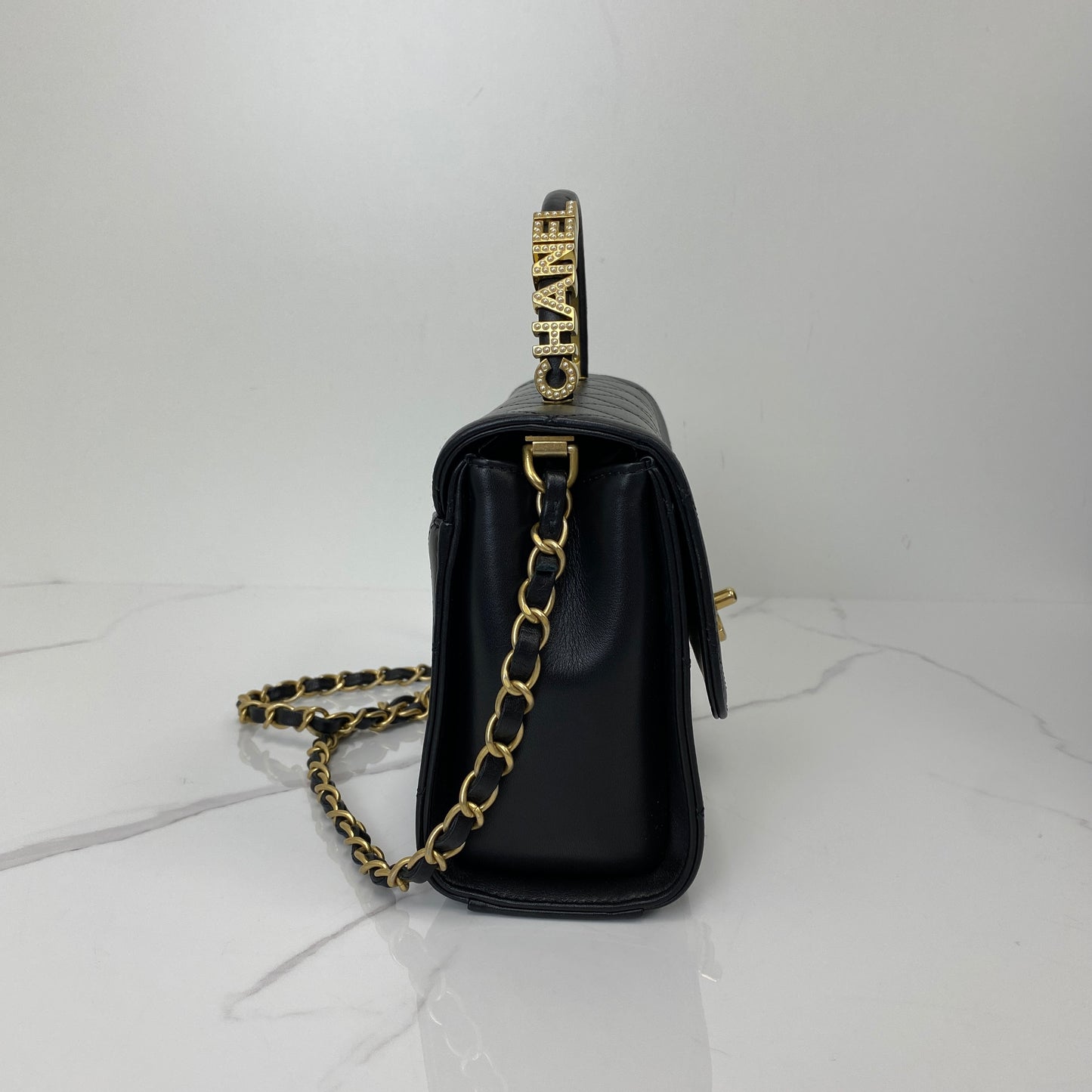 Side view showing the Chanel logo-lettered top handle and leather-woven chain